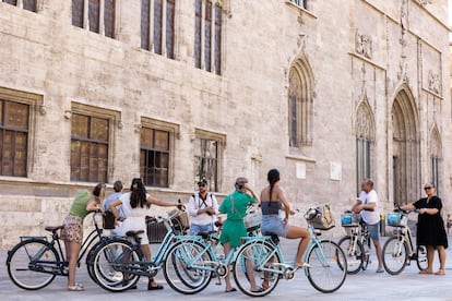 Un grupo de turistas en bicicleta escucha las explicaciones de su guía ante el edificio de La Lonja en el centro histórico de València, este martes uno de agosto.