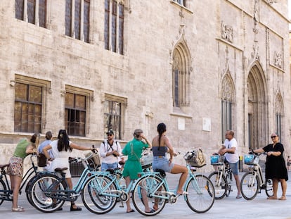 Un grupo de turistas en bicicleta escucha las explicaciones de su guía ante el edificio de La Lonja en el centro histórico de València, este martes uno de agosto.