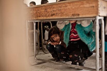 Nour se esconde debajo del pupitre al escuchar el paso de un helicóptero en una escuela clandestina de Alepo (Siria).
