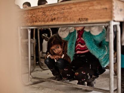 Nour se esconde debajo del pupitre al escuchar el paso de un helicóptero en una escuela clandestina de Alepo (Siria).