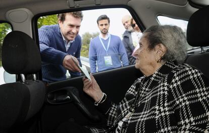 Una anciana de 98 años, ante la imposibilidad de acceder al colegio electoral, ejerce su derecho al voto entregando su papeleta al presidente de la mesa desde el coche, en el municipio sevillano de Tomares.