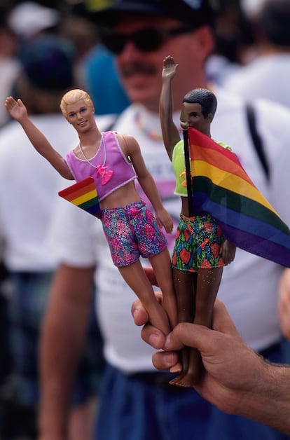 A man holds two Ken dolls with rainbow flags during the celebration of the twenty-fifth anniversary of the Stonewall uprising.