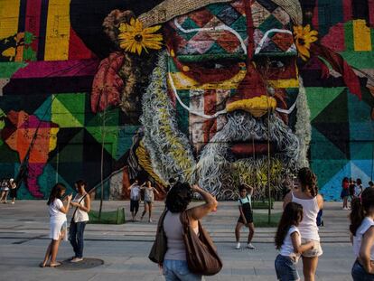 Pessoas caminham pela orla do porto, em frente ao grafite do artista Eduardo Kobra.