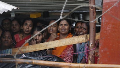 Varias mujeres se protegen de la lluvia bajo un tejado mientras observan las labores de rescate tras derrumbarse un muro en Bombay (India), este martes. Al menos 15 personas han muerto tras el siniestro provocado por las fuertes precipitaciones que ha traído este año el monzón.