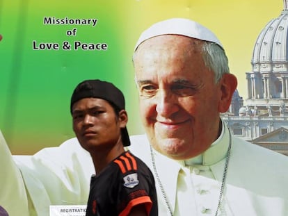 Um homem passa diante de um anúncio da viagem do Papa em Yangon.
