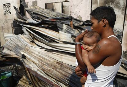 Un hombre con su bebé entre los materiales recuperados después de un incendio en el barrio de Malabon, en Manila, Filipinas.