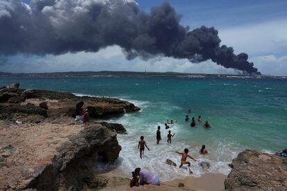 Un grupo de personas disfruta de un día de playa cerca del humo del incendio sobre los tanques de almacenamiento de combustible que explotaron cerca del puerto de supertanqueros en Matanzas.