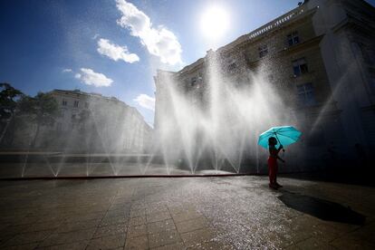 Una niña con un paraguas se coloca bajo los rociadores de agua durante una ola de calor en Viena (Austria).