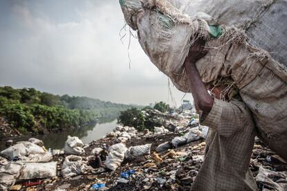 A orillas del río Mithi, en Bombay (India), hay quienes se ganan la vida buscando metal entre la basura que ya ha sido previamente reciclada. Esta es una opción pestilente e insalubre que para algunos es la única manera de ganarse la vida. En la imagen, uno de los 'recicladores' traslada un saco lleno de plástico hacia la orilla.