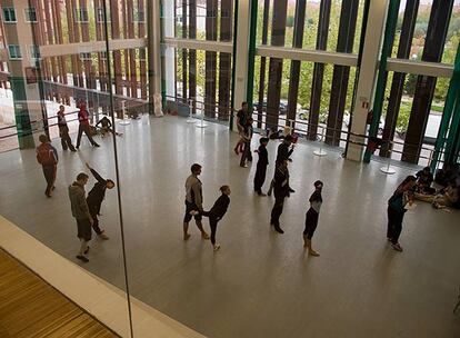 Los bailarines de la compañía se dispersan por la sala de ensayos para poder moverse con comodidad, mientras siguen atentos las indicaciones de la directora. Los que no trabajan, observan desde una esquina la evolución de sus compañeros y disfrutan de algún tentempié.