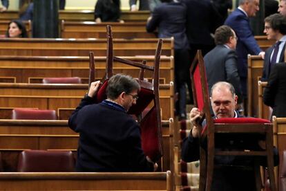 Dos ujieres colocan sillas en el hemiciclo del Congreso de los Diputados poco antes del comienzo de la primera jornada de investidura de Pedro Sánchez como presidente del Gobierno.