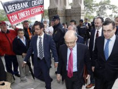 El ministro de Hacienda, Cristóbal Montoro, pasa junto a un un grupo de afectados por las preferentes que se concentraron a la entrada de la Universidad Internacional Menéndez Pelayo donde hoy se celebró el seminario " Competitividad y Marca España ".