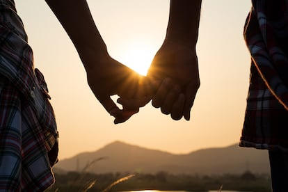 Close up of loving couple holding hands while walking at sunrise sunset in the meadow mountain in background. Valentine’s Day and love concept.