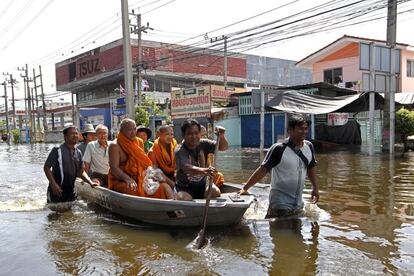 Tres monjes budistas son transportados, junto a otras personas, por una calle inundada en las afueras de Bangkok