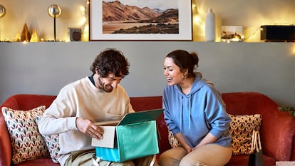 Un hombre abriendo un regalo que le da una chica en un salón.