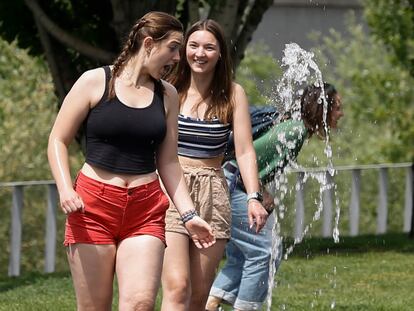 Dos jóvenes se refrescan con una fuente en Madrid.