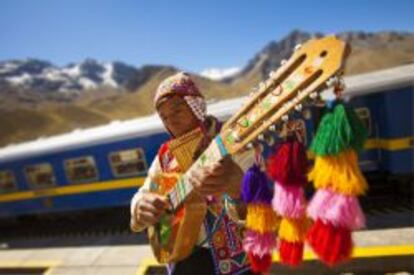 Un nativo del Cuzco toca la quena y la bandurria, instrumentos musicales andinos. Al fondo, el tren Hiram Bingham.