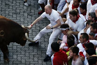 Un mozo agarra por el cuerno a un toro de la ganadería de Alcurrucén, que se quedo rezagado, en el recorrido del primer encierro de San Fermín.