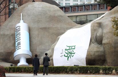 La gente observa una estatua gigante tumbada con la vacuna y con una mascarilla en la que puede leerse en mandarín "triunfo" en Daegu, Corea del Sur.