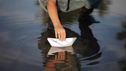 Un niño deposita un barco de papel en el agua.
