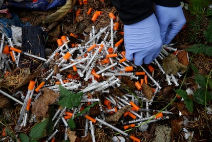 A volunteer cleans up needles used for drug injection that were found at a homeless encampment in Everett, Wash