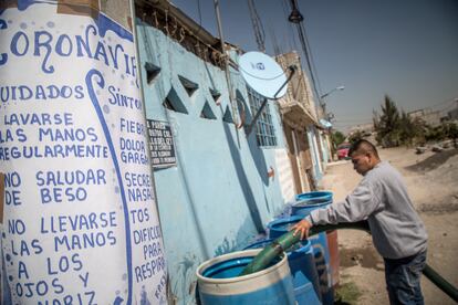 Un hombre rellena cubos de agua, frente a un cartel sobre el coronavirus en Rubén Jaramillo.