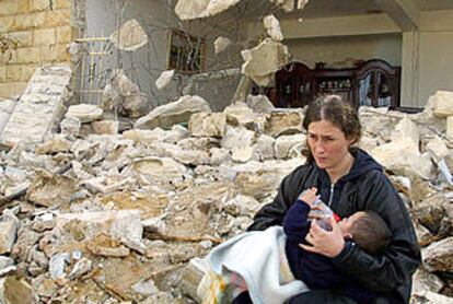 Una mujer palestina alimenta a su hijo frente a su casa, destruida por los ataques israelíes.