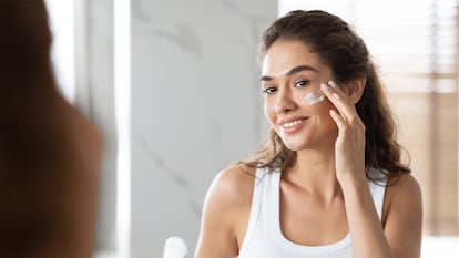 Una chica aplicándose crema enfrente de un espejo