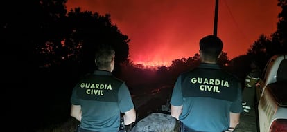 Dos agentes de la Guardia Civil contemplan las llamas durante los trabajos nocturnos de lucha contra el fuego en el incendio de Porto (Zamora).