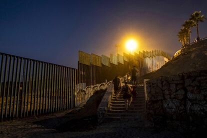 La gente pasa junto a la valla fronteriza al salir de la playa Tijuana en Baja California (México).