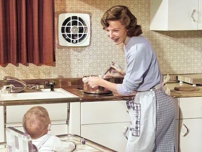 Una mujer cocina para su familia mientras cuida su hijo bebé en 1950.