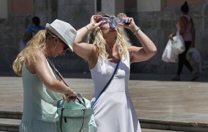 Dos turistas que visitan Valencia alivian el calor con agua.