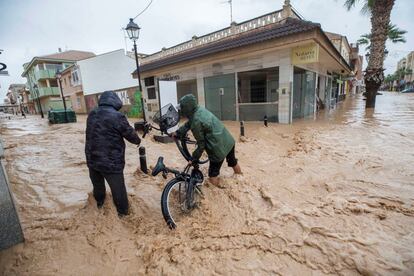 Dos vecinos de Los Alcázares en Murcia intentan cruzar con su bicicleta una calle inundada a causa de las fuertes lluvias en el Campo de Cartagena. 