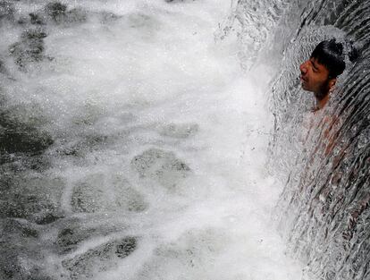 Un chico se refresca bajo una cascada para combatir el calor a las afueras de Srinagar, Cachemira (India).