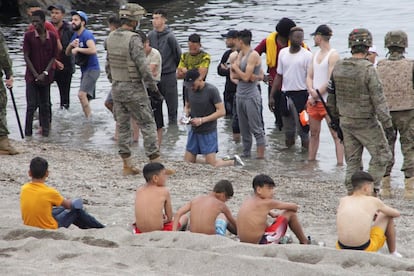 Na praia do Tarajal, há grupos de jovens de pé, na água, em frente aos militares, que formaram um cordão na orla.