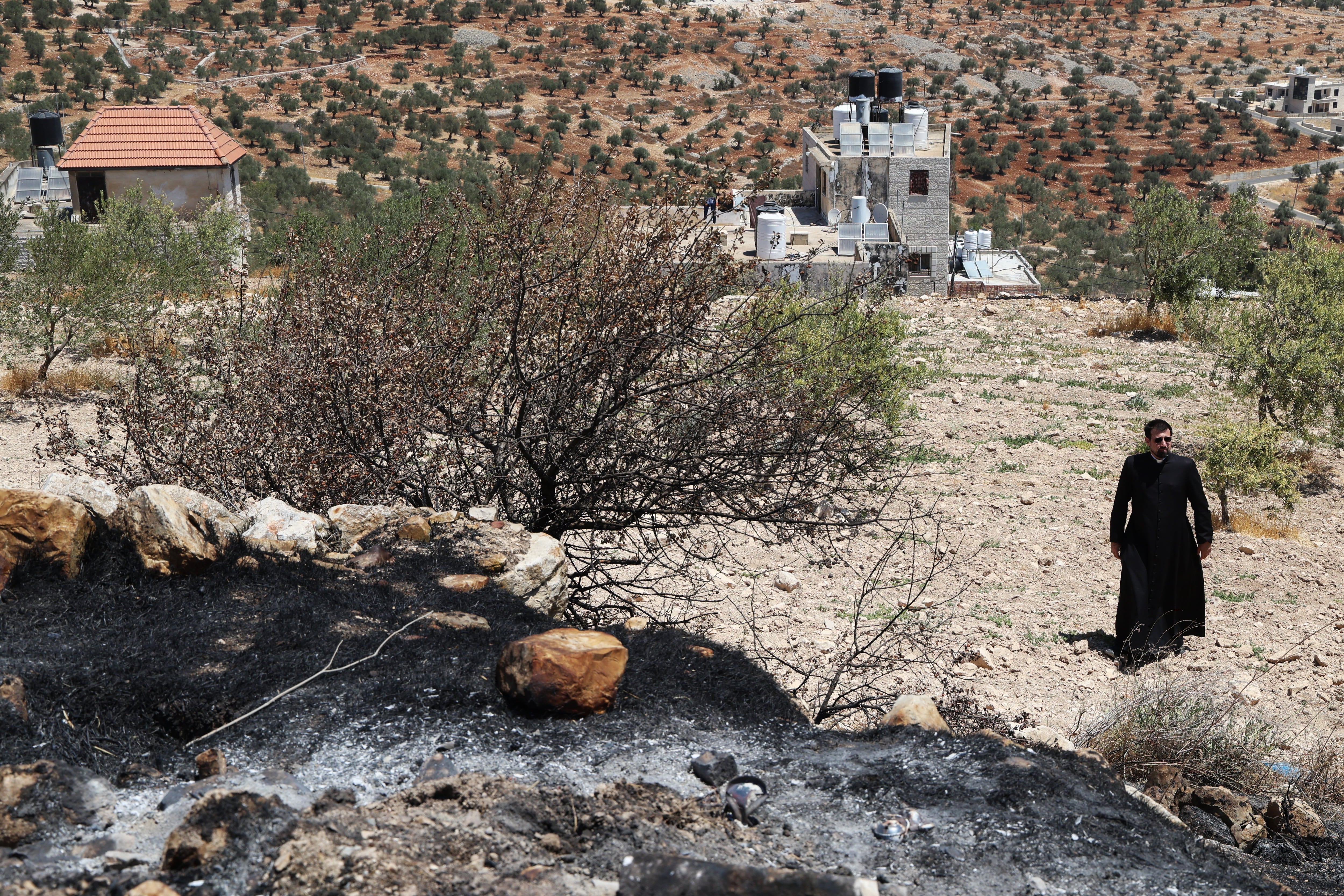 Un sacerdote, este lunes, junto a parte del terreno quemado por colonos judíos junto a la iglesia de San Jorge de Taybeh (Cisjordania).