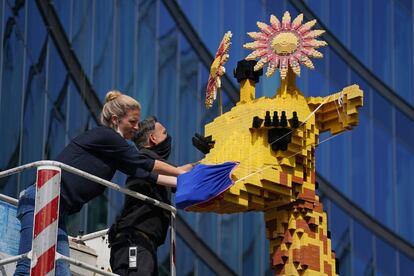 Dos operarios ponen una mascarilla protectora a una jirafa de 7 metros de altura hecha con piezas de lego en el parque temático Legoland, en Berlín, antes de su reapertura. Alemania ha levantado la mayoría de restricciones al movimiento que habían sido impuestas para evitar la propagación de la pandemia.