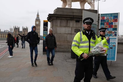 Um policial carrega floresna ponte de Westminster, reaberta nesta quinta.