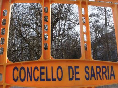 Valla de obra en Sarria, con &aacute;rboles pendientes de tala al fondo.