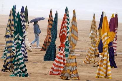 Paseante con paraguas entre la bruma y las sombrillas cerradas de la playa de San Lorenzo de Gijón, el pasado viernes 7 de junio.