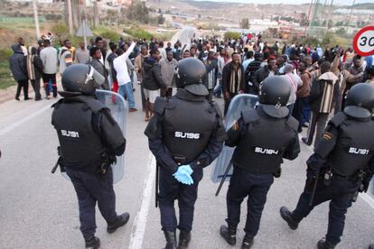 Policías antidisturbios ante el grupo de inmigrantes alojados en el centro de internamiento que han animado a sus compañeros subidos a la verja fronteriza de Melilla.