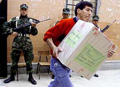 Un funcionario porta una urna al interior de un colegio electoral de Lima en presencia de varios militares.