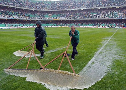 Operarios del Betis intentan retirar el agua del césped.