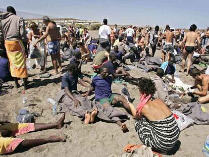 Turistas e inmigrantes, que acaban de llegar en una patera, se mezclan en la playa de Tejita, en Granadilla (Tenerife).