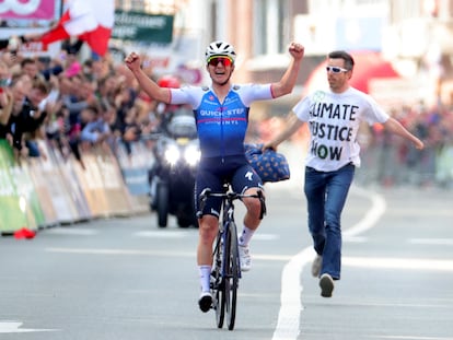 Evenepoel cruza ganador la meta de la Lieja-Bastogne-Lieja ante un activista contra el cambio climático.