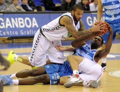 Woods disputa desde el suelo un balón con dos jugadores de Unicaja.