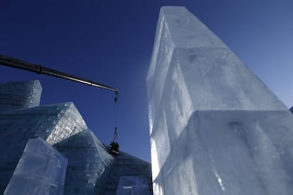 Una grúa coloca un gran bloque de hielo en uno de los edificios que forman parte del festival de Harbin.