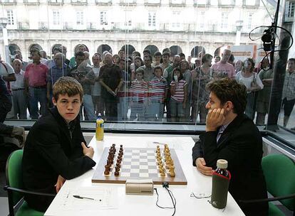 Magnus Carlsen y Levon Aronián aguardan a que comiencen las partidas. Detrás de   la urna, un nutrido grupo de aficionados.