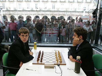 Magnus Carlsen y Levon Aronián aguardan a que comiencen las partidas. Detrás de la urna, un nutrido grupo de aficionados.