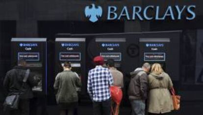 Unas personas retiran dinero de unos cajeros automáticos en el exterior de una sucursal del banco británico Barclays en Londres, Reino Unido. EFE/Archivo
